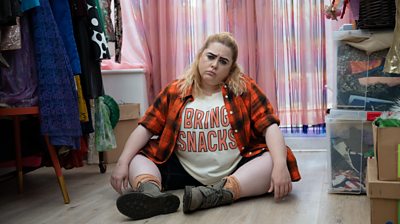 Patsy Lowe as Sal sitting on the floor of a dressing room with a sad face wearing a t-shirt that says Bring Snacks