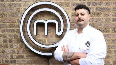 Man wearing MasterChef branded t-shirt in front of MasterChef logo looking at camera