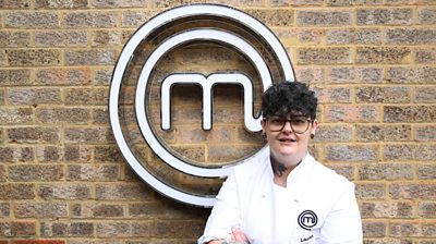 Woman wearing MasterChef branded t-shirt in front of the MasterChef logo smiles at the camera