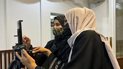 Two women wearing head coverings, work with a mobile phone on a journalism training course. 