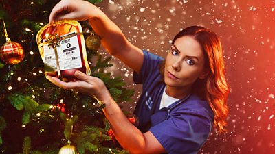 Stevie, a woman in hospital scrubs, hangs a bag of blood on a Christmas tree