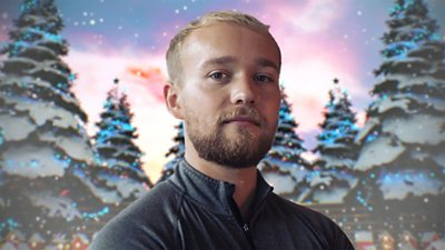 Billy Monger wears a grey top and is pictured, head and shoulders, against a backdrop of animated, snowy Christmas trees