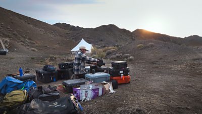 a cameraman preparing a camera in the desert surrounded by equipment