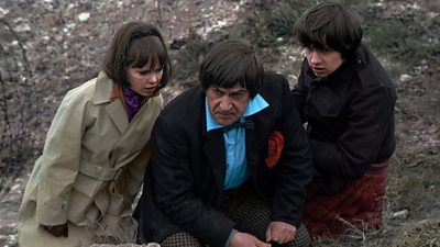 The Doctor and his companions, Jamie McCrimmon and Zoe Heriot crouch down on a battlefield