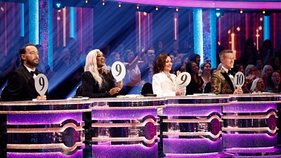 The Strictly Come Dancing judges sit behind their bright tables, holding their paddles aloft. Craig, Motsi and Shirley hold up the number 9 paddle while Anton holds up a 10 paddle.