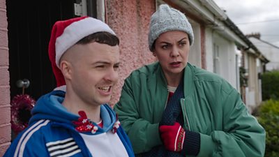 Conor and Mairéad stand outside in festive winter hats and jackets