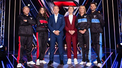 Left to right: Rob Beckett, Ellie Taylor, Bradley Walsh, Barney Walsh, Louise Minchin and Joel Dommett all stand on the Gladiators stage with the celebrities in black tracksuits with blue and red stripes