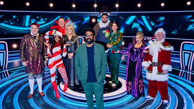 Host Romesh Ranganathan and contestants in costume. The contestants are Tim Vine (Ebeneezer Scrooge), Indiyah Polack (Candy Cane), Phil Tufnell (Poinsettia), Sally Lindsay (Angel/Fairy), Hasan Semay (Reindeer), Heather Peace (Christmas Tree), Kerry Katona (Wicked Witch) and Shaun Ryder (Santa Claus)