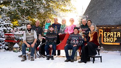 The Repair Shop team sit and stand around a sled in a snowy scene outside the Repair Shop barn. People: Bottom row: Dom Chinea, Pierro Pozella, Pete Woods, Suzie Fletcher Top row: Steve Fletcher, Kirsten Ramsay, Brenton West, Julie Tatchell, Amanda Middleditch, Mark Stuckey, Will Kirk