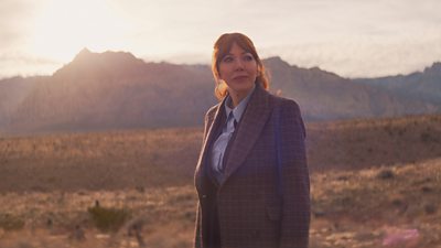 Philomena Cunk (Diane Morgan) wanders in a dry, arid landscape with mountains in the background