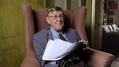 Alan Bennett sits in an armchair holding some papers