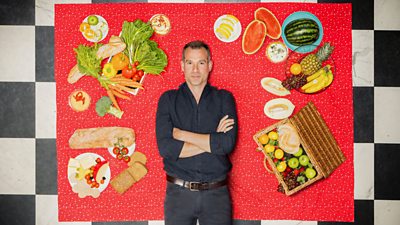 Dr Chris van Tulleken lies on a red picnic blanket surrounded by different foods