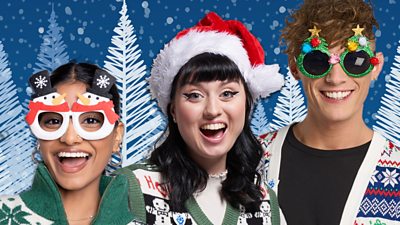 Blue Peter presenters in Christmas jumpers and hats and glasses smiling to camera