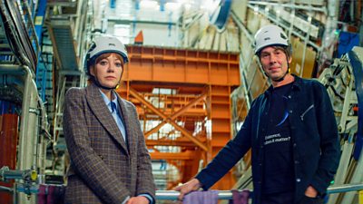 Philomena Cunk (Diane Morgan) and Brian Cox wearing hard hats surrounded by scaffolding and equipment