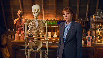 Philomena Cunk (Diane Morgan) standing next to a skeleton in an old-fashioned laboratory 