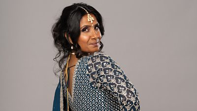 Suki poses looking back over her shoulder, wearing a traditional dress of dark blue with silver pattern