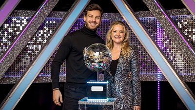 Vito and Sarah stand together behind the Strictly Come Dancing glitterball trophy in the It Takes Two studio