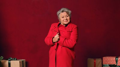 Barbara Flynn is pictured against a red background, wrapped up in a red coat