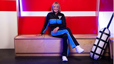 Louise Minchin sits on a wooden bench in a changing room, smiling for the camera