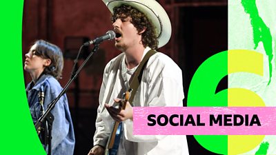 The lead singer sings into a microphone while playing guitar wearing a white jacket and cowboy hat. There is text in the bottom right saying 'Social Media'.