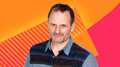 Mark Radcliffe smiles at the camera in front of a pink and orange patterned background