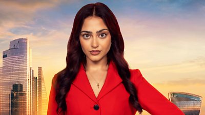 Amber wears a red suit with big black buttons and a gold necklace. Her long curled hair drapes over each shoulder. A backdrop of the London skyline at sunset 