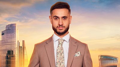 Carlo wears a brown suit with a matching floral tie and pocket square. He has a full beard and raises an eyebrow to camera. A backdrop of the London skyline at sunset 