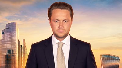 Dean wears a navy suit with a beige patterned tie and white shirt. His hair is combed back. A backdrop of the London skyline at sunset 