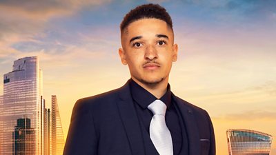 A young looking Jordan wears a navy three piece suit with a navy shirt and white tie. Jordan has a thin moustache. A backdrop of the London skyline at sunset 