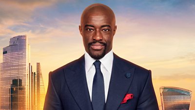 Tim Campbell in a blue suit with a red handkerchief in his jacket pocket. He stands front of a backdrop of the London skyline