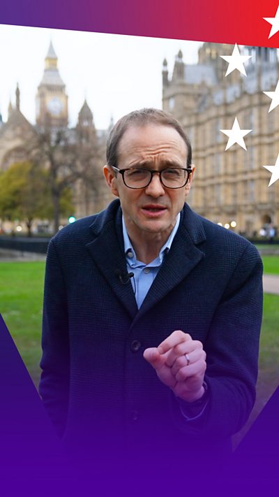 Chris Mason wearing a shirt and coat stood on the College Green grass in front of the UK Houses of Parliament