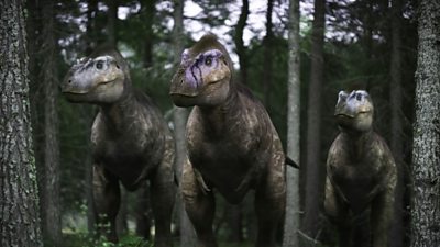 Three dinosaurs walk on their hind legs through a forest.