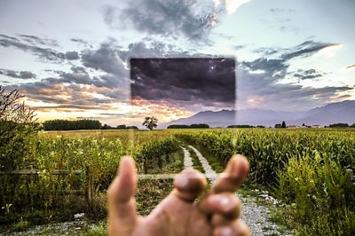 Photo of person holding up a frame of glass to clouds in the sky.