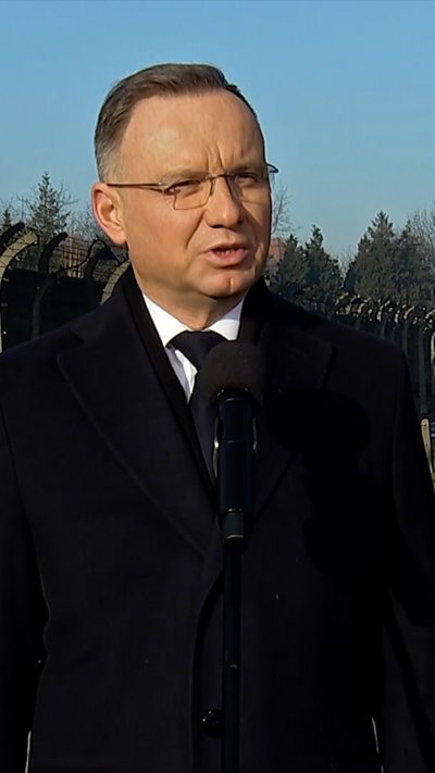 Andrzej Duda delivering speech at Auschwitz. He is wearing a thick black coat on top of a suit, white shirt and black tie