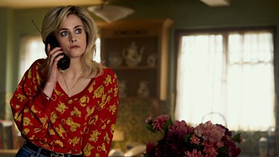 Stefanie Martini in character as Marnie Palmer on set of The Gold wearing a red blouse with a gold lion pattern.  She is on the phone