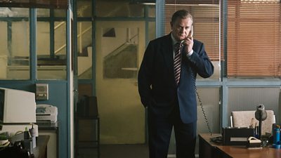 Hugh Bonneville  in character and on set as Brian Boyce. He is on the telephone in an office