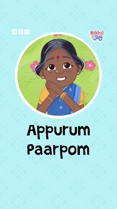 A elderly south Indian woman with silver in her hair holds her clasped hands to her cheek, smiling happily.