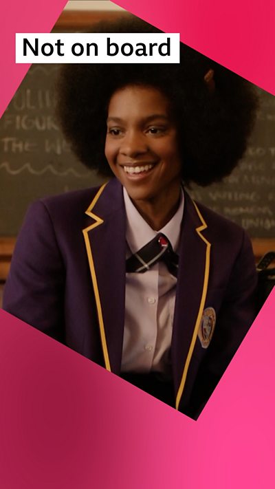 A girl in school uniform sits in a classroom, she wears a purple blazer with a white shirt and has black Afro hair