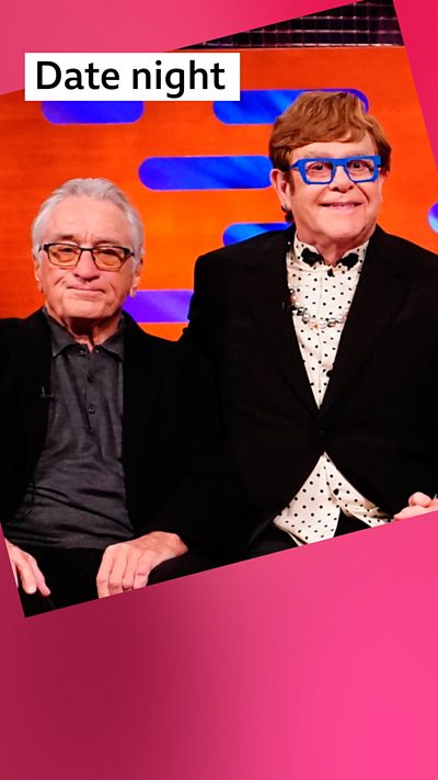 Robert De Niro and Elton John sat side-by-side, both wearing black jackets and glasses