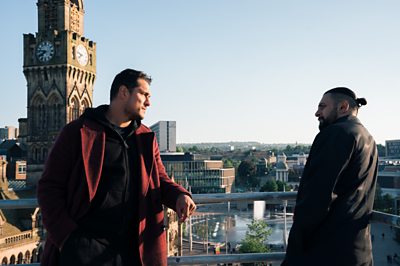 An image of Harry Virdee (STAZ NAIR) and Riaz Hyatt (VIKASH BHAI) looking out over a vista of Bradford from the Drama series, Virdee