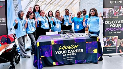 A group of people behind a booth that says "launch your career at the BBC"