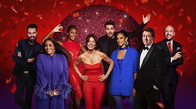 The presenters stood wearing smart clothes in front of a red shiny and glittery backdrop with confetti