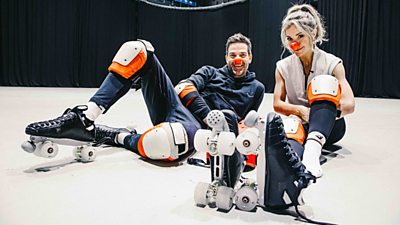 Gethin Jones and Helen Skelton sat on the floor in a studio wearing roller skates, shin pads and red noses