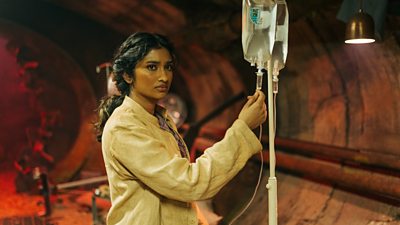 A woman stands holding a line to a drip, looking concerned