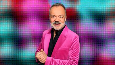 A head and shoulders shot of presenter Graham Norton, smiling for the camera wearing a pink jacket over a black shirt