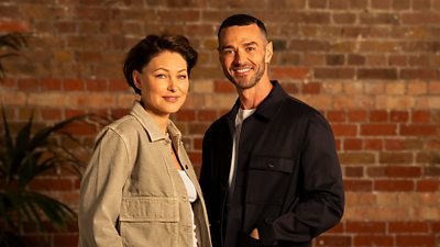 Emma and Matt Willis stood together in front of an exposed brick wall smiling