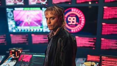 A human-like character with horns stands by a control desk looking suspicious