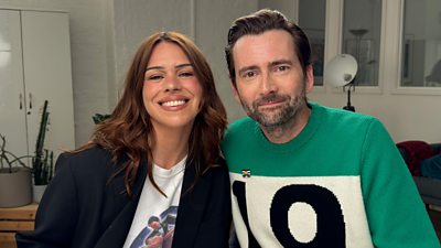 Billie Piper and David Tennant sit side by side smiling