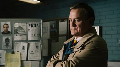 Hugh Bonneville in character as Brian Boyce, stood in a dark office, with crime reports on a pin board behind him