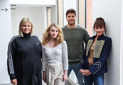 A group shot of four actors stood by a window smiling at the camera